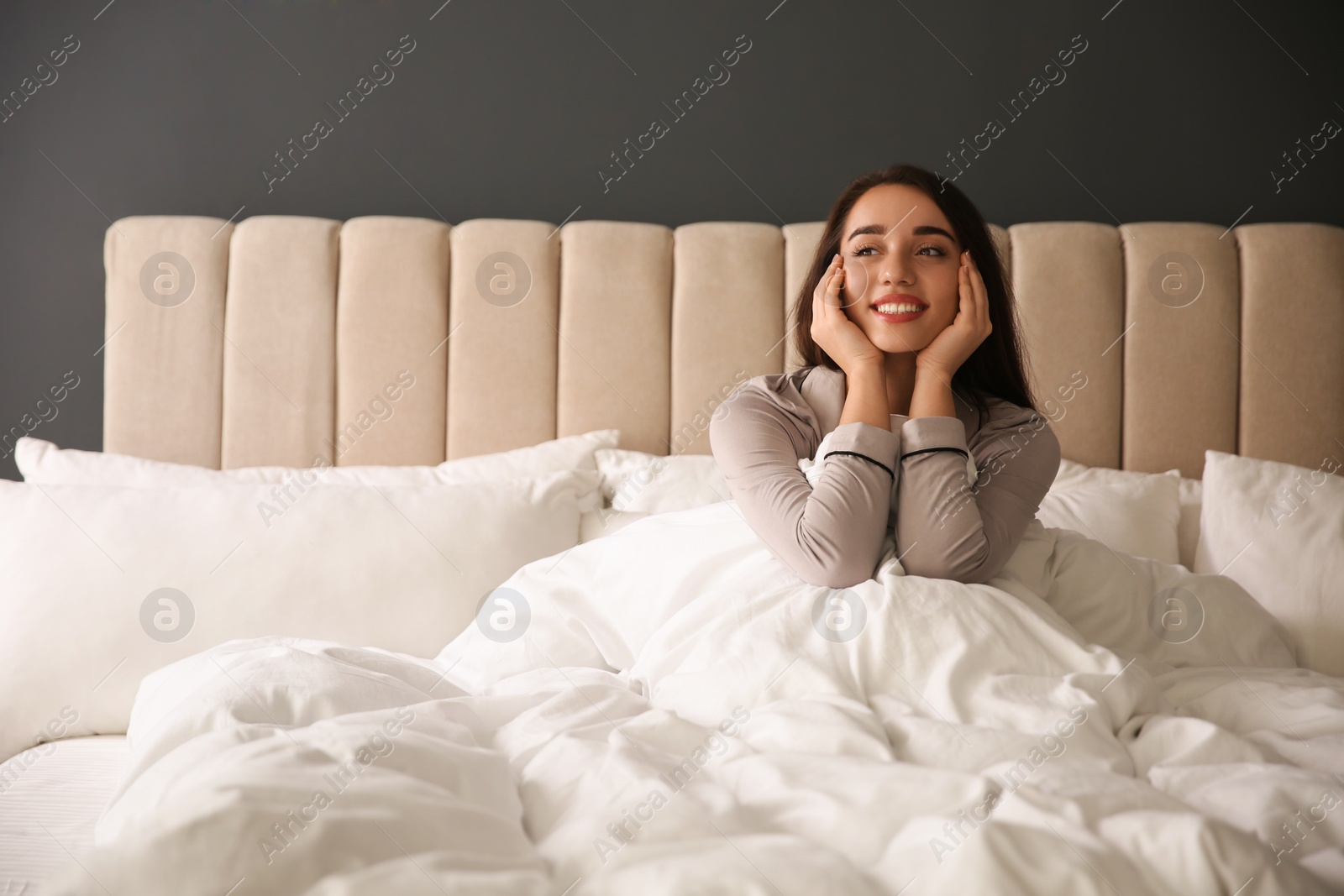 Photo of Beautiful young woman wrapped with soft blanket relaxing on bed at home