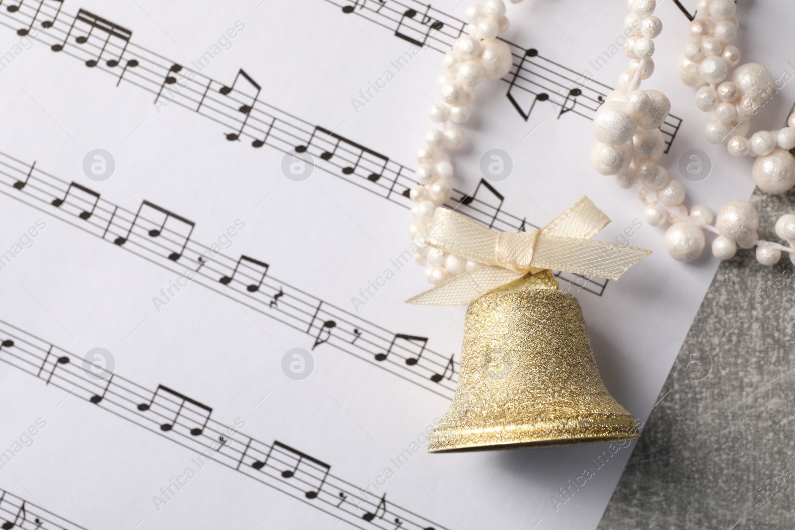 Photo of Golden shiny bell with bow and music sheet on light gray table, flat lay. Space for text. Christmas decoration