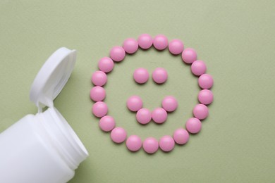 Happy emoticon made of antidepressants and medical bottle on light green background, flat lay