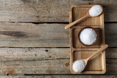 Photo of Organic salt in bowl and spoons on wooden table, top view. Space for text