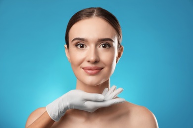 Doctor examining woman's face before plastic surgery on light blue background