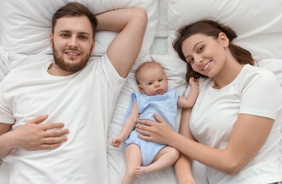 Happy family. Parents with their cute baby on bed, top view