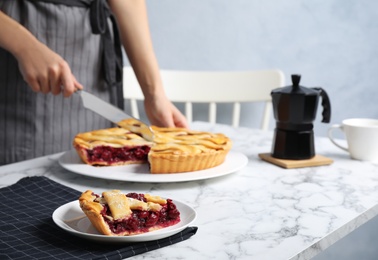 Photo of Closeup view of woman cutting tasty cherry pie at white marble table, focus on plate with slice