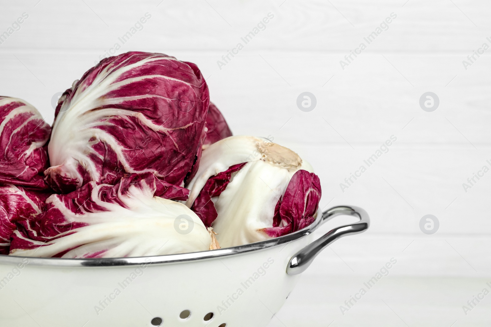 Photo of Fresh ripe radicchios in colander on white background, closeup. Space for text