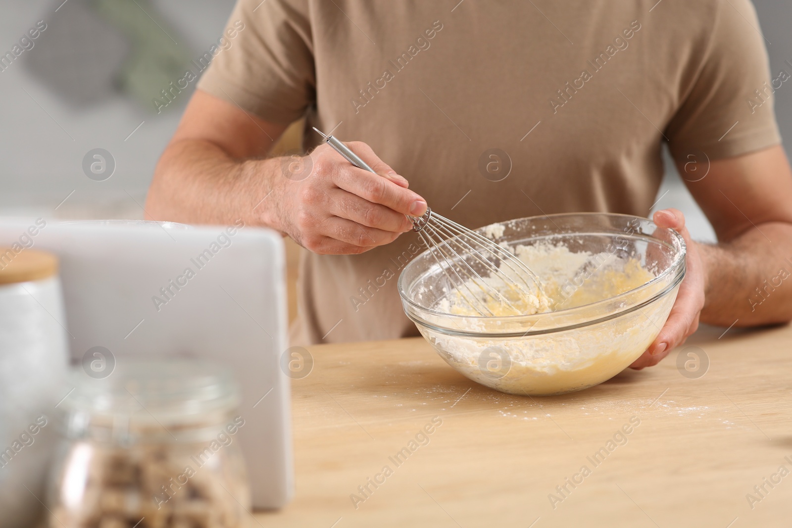 Photo of Man making dough while watching online cooking course via tablet in kitchen, closeup