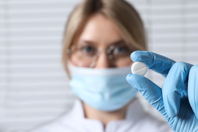 Photo of Doctor holding pill on light background, selective focus. Space for text