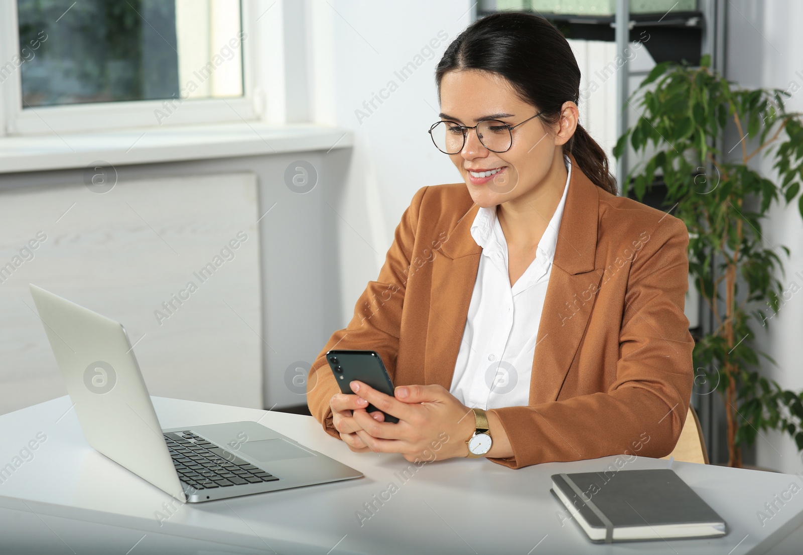 Photo of Young woman using smartphone at table in office