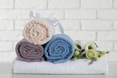 Photo of Rolled and folded towels with flowers on white table, closeup
