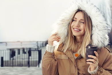 Young woman with cup of coffee walking outdoors. Space for text