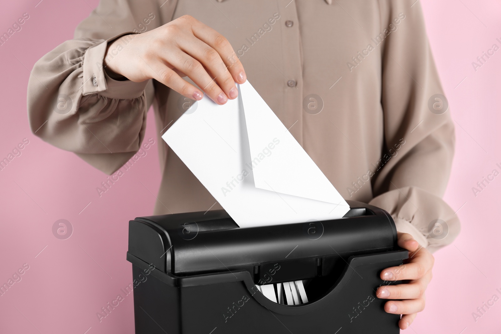 Photo of Woman destroying envelope with shredder on pink background, closeup