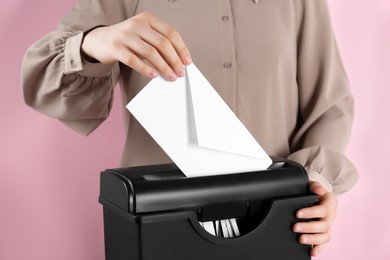 Woman destroying envelope with shredder on pink background, closeup