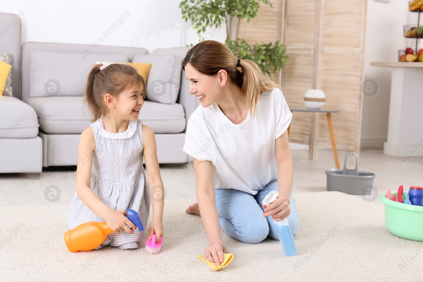 Photo of Housewife with daughter cleaning carpet in room together