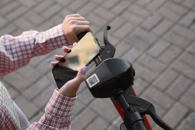 Photo of Woman using smartphone to pay and unblock electric kick scooter outdoors, closeup