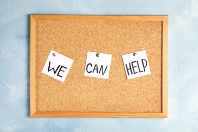Cork bulletin board with pinned words "WE CAN HELP" hanging on color wall