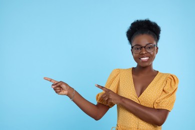 Photo of Beautiful young woman in eyeglasses pointing at something on light blue background, space for text