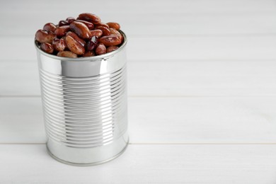 Photo of Tin can with kidney beans on white wooden table, space for text