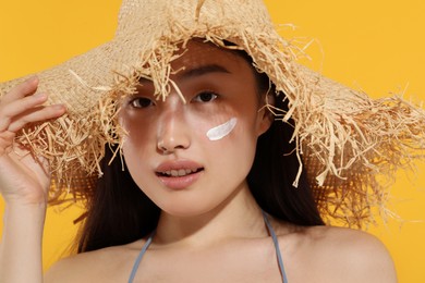 Photo of Beautiful young woman in straw hat with sun protection cream on her face against orange background