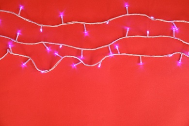 Glowing Christmas lights on color background, top view