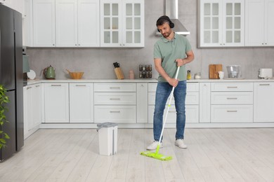 Photo of Enjoying cleaning. Man in headphones listening to music and mopping floor in kitchen