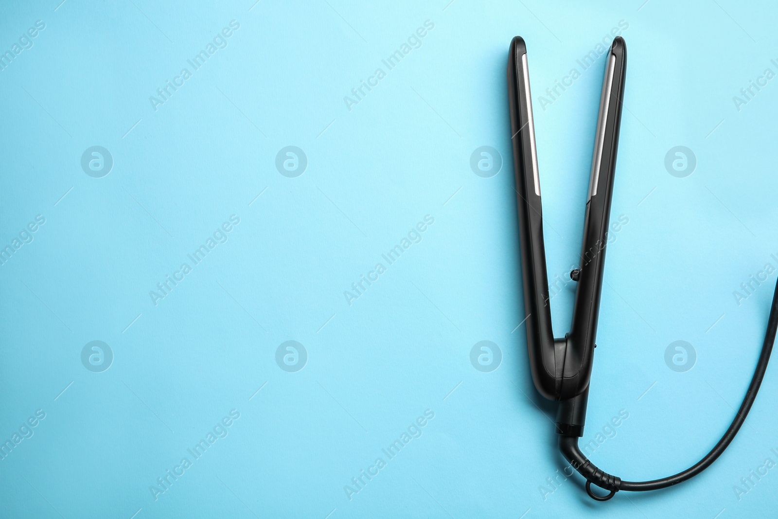 Photo of Modern flat hair iron on light blue background, top view. Space for text