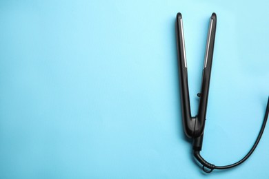 Photo of Modern flat hair iron on light blue background, top view. Space for text