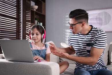 Photo of Internet addiction. Man scolding his daughter while she using laptop in living room