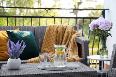 Rattan table with jug of water, glasses and beautiful flowers on terrace