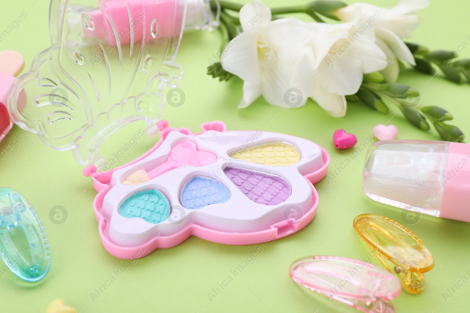 Photo of Decorative cosmetics for kids. Eye shadow palette, accessories and flowers on light green background, closeup