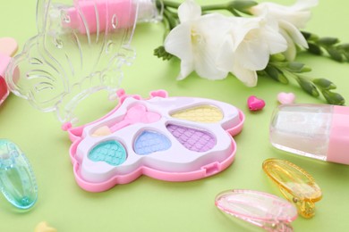 Photo of Decorative cosmetics for kids. Eye shadow palette, accessories and flowers on light green background, closeup