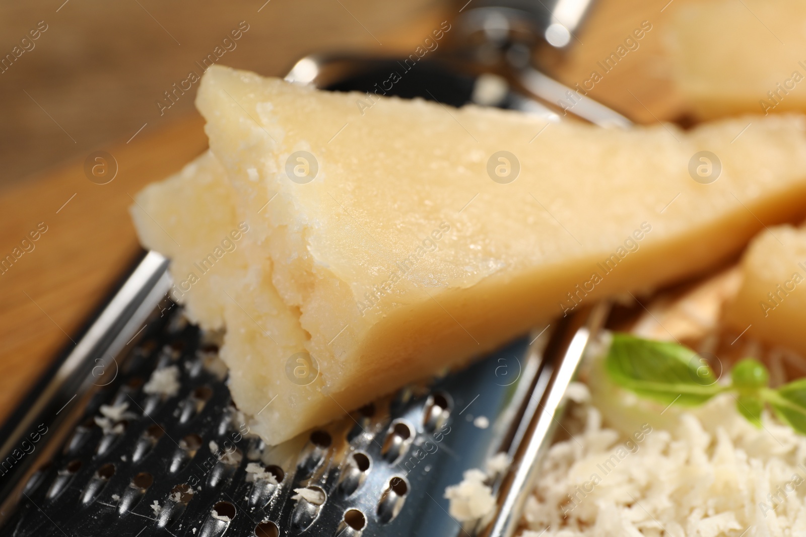 Photo of Grated parmesan cheese with basil near grater, closeup