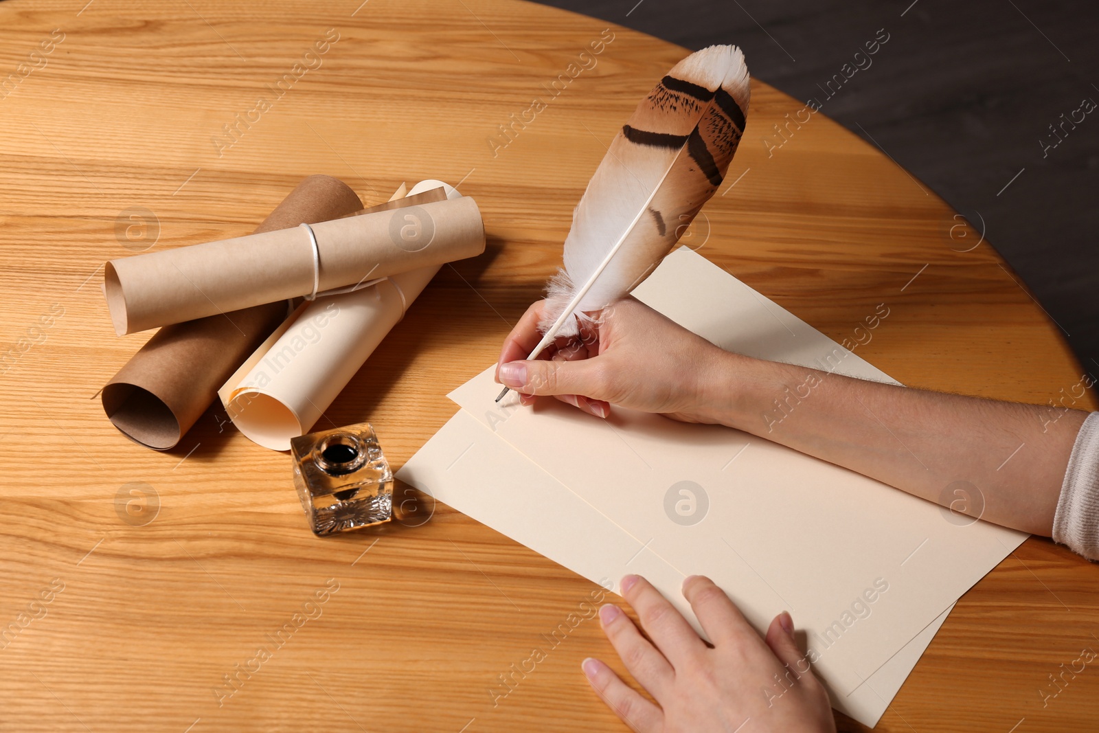 Photo of Woman using feather pen to write with ink on parchment at wooden table, closeup