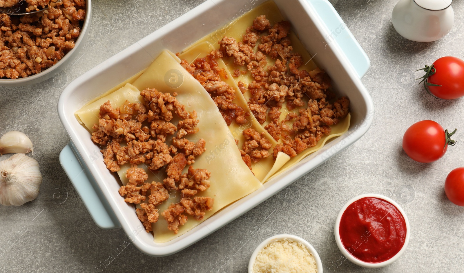 Photo of Cooking lasagna. Pasta sheets, minced meat in baking tray and products on light textured table, flat lay