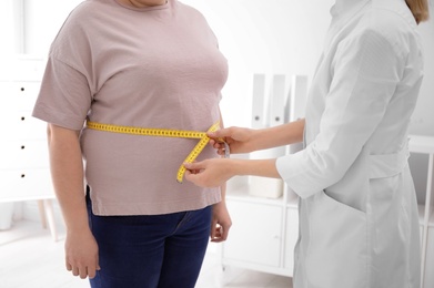 Photo of Doctor measuring waist of overweight woman in clinic, closeup