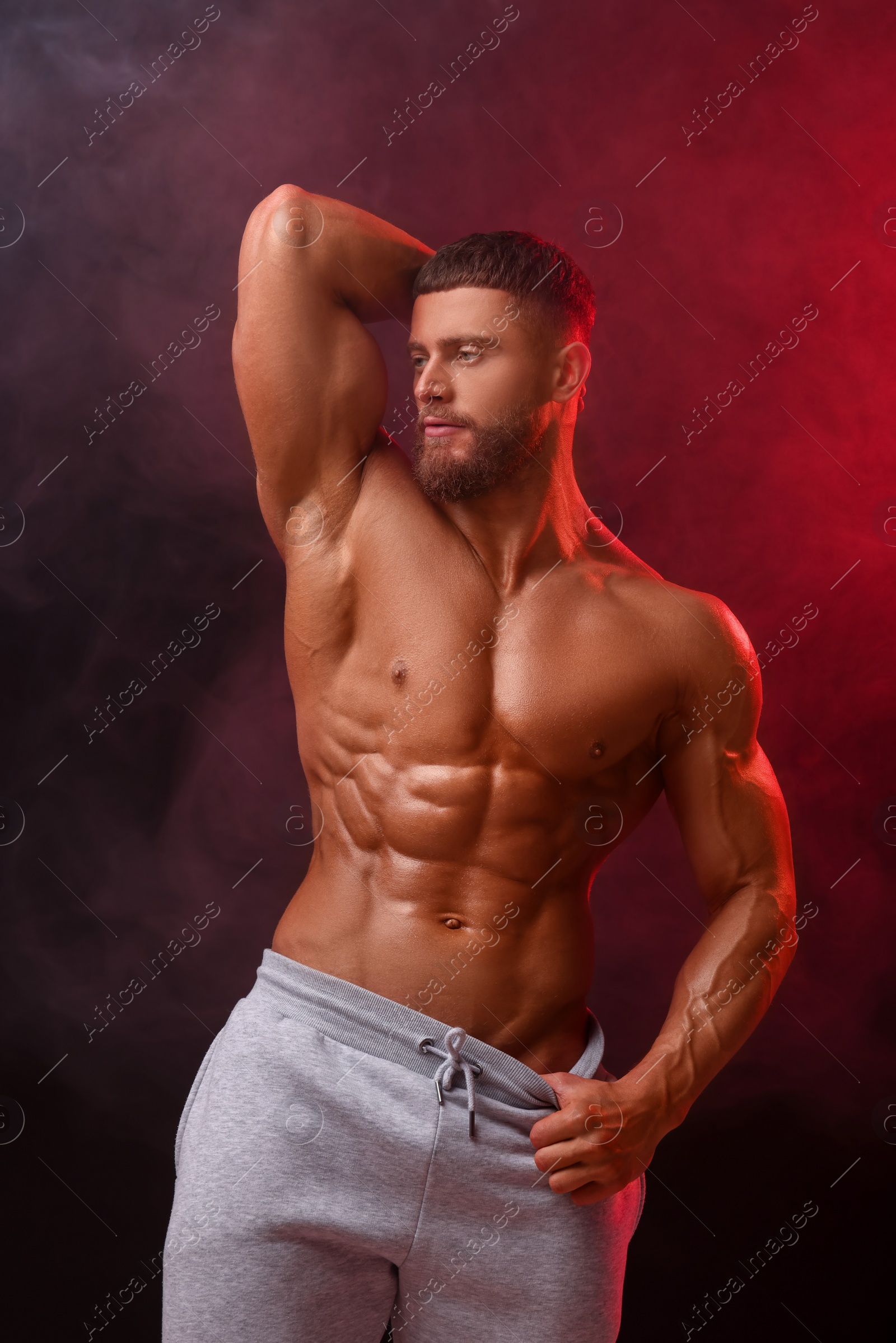 Photo of Young bodybuilder with muscular body in smoke on color background