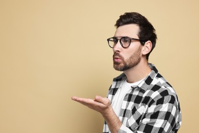 Handsome man blowing kiss on beige background. Space for text