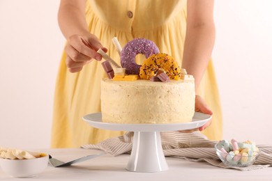 Photo of Woman decorating delicious cake with sweets at white wooden table, closeup
