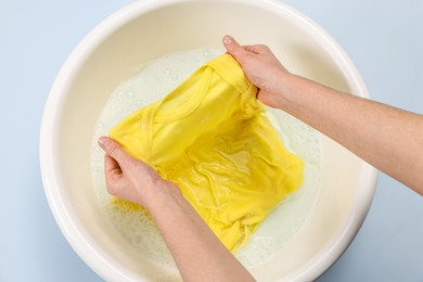 Photo of Woman washing baby clothes in basin on light blue background, top view