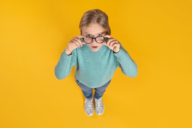 Photo of Cute girl in glasses on orange background, above view