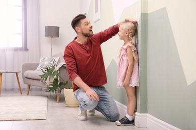 Photo of Young man measuring his daughter's height at home