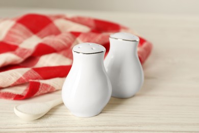 Photo of Ceramic salt and pepper shakers, spoon with napkin on white wooden table, closeup