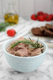 Photo of Bowl with canned tuna and rosemary on white marble table, closeup