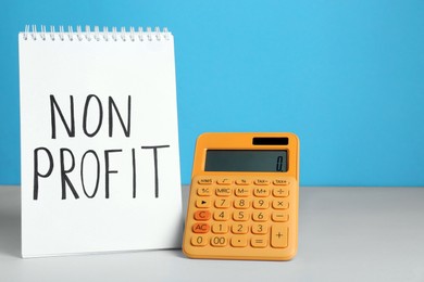 Photo of Notebook with phrase Non Profit and calculator on white table. Space for text