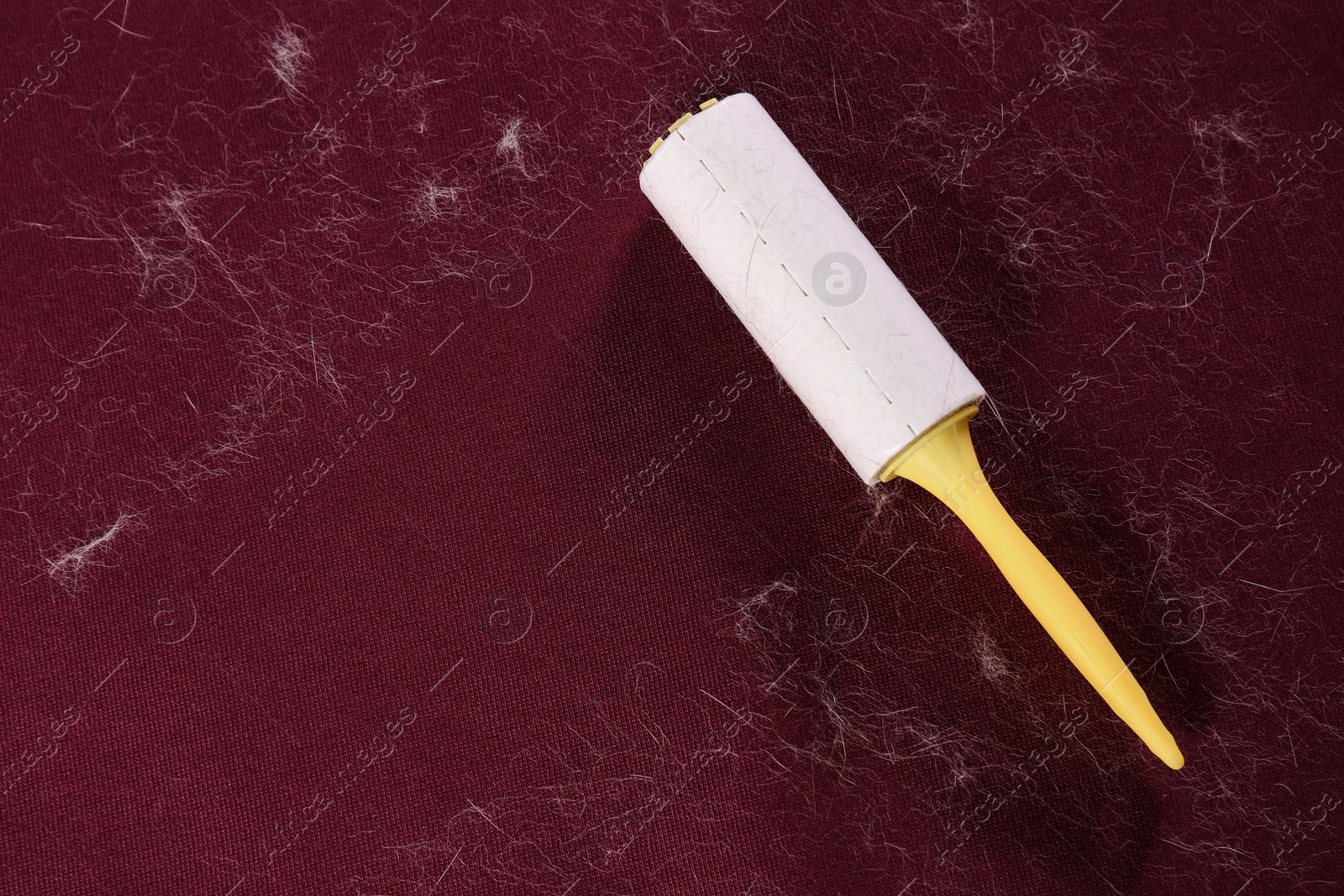 Photo of Lint roller on red fabric covered with hair, top view. Space for text