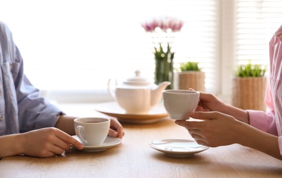 Photo of Women with cups of tea at table near window indoors, closeup
