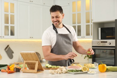 Photo of Man making dinner while watching online cooking course via tablet in kitchen