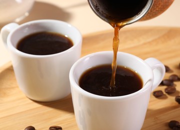 Photo of Pouring aromatic coffee from cezve into cup at wooden board, closeup