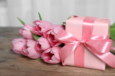 Photo of Gift box and beautiful tulip flowers on wooden table, closeup