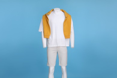 Photo of Male mannequin dressed in white t-shirt, stylish shorts and orange sweater on light blue background