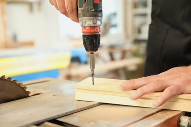 Photo of Working man using electric screwdriver at carpentry shop, closeup