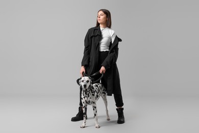 Beautiful young woman with her adorable Dalmatian dog on light grey background. Lovely pet